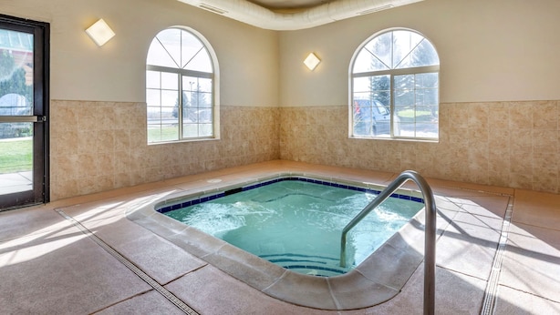 A hot tub in a room with two arched windows, beige walls, and a tiled floor. - Comfort Inn Evansville - Casper (Evansville)