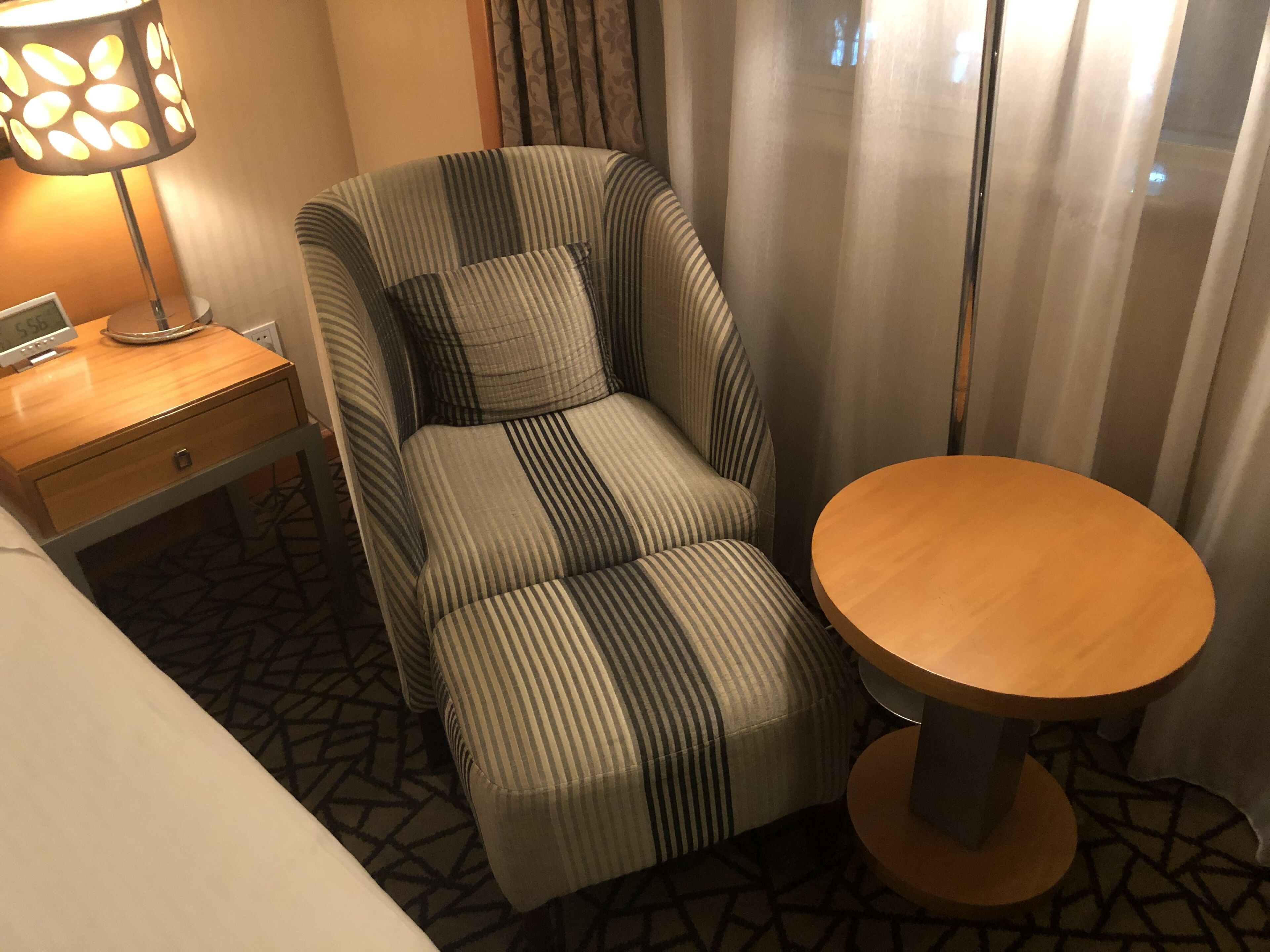 A hotel room with a striped armchair, a small wooden table, and a nightstand with a lamp.