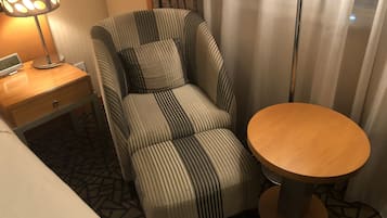 Ein Hotelzimmer mit einem gestreiften Sessel, einem kleinen Holztisch und einem Nachttisch mit Lampe.