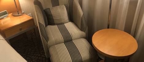 A hotel room with a striped armchair, a small wooden table, and a nightstand with a lamp.