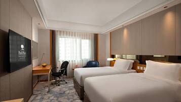 A hotel room with two beds, a desk with a chair, a TV, and a window with curtains.