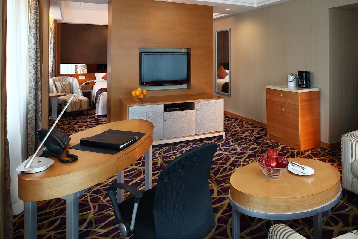Een hotelkamer met een bureau, stoel, televisie, minibar en een klein zithoekje.