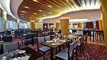 A spacious hotel dining area with multiple tables and chairs, a central bar, and a modern ceiling design.