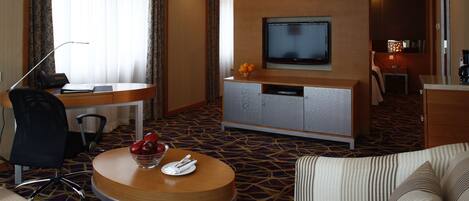 A hotel room with a TV, a desk, a dining area, and a seating area with a small table and chairs.