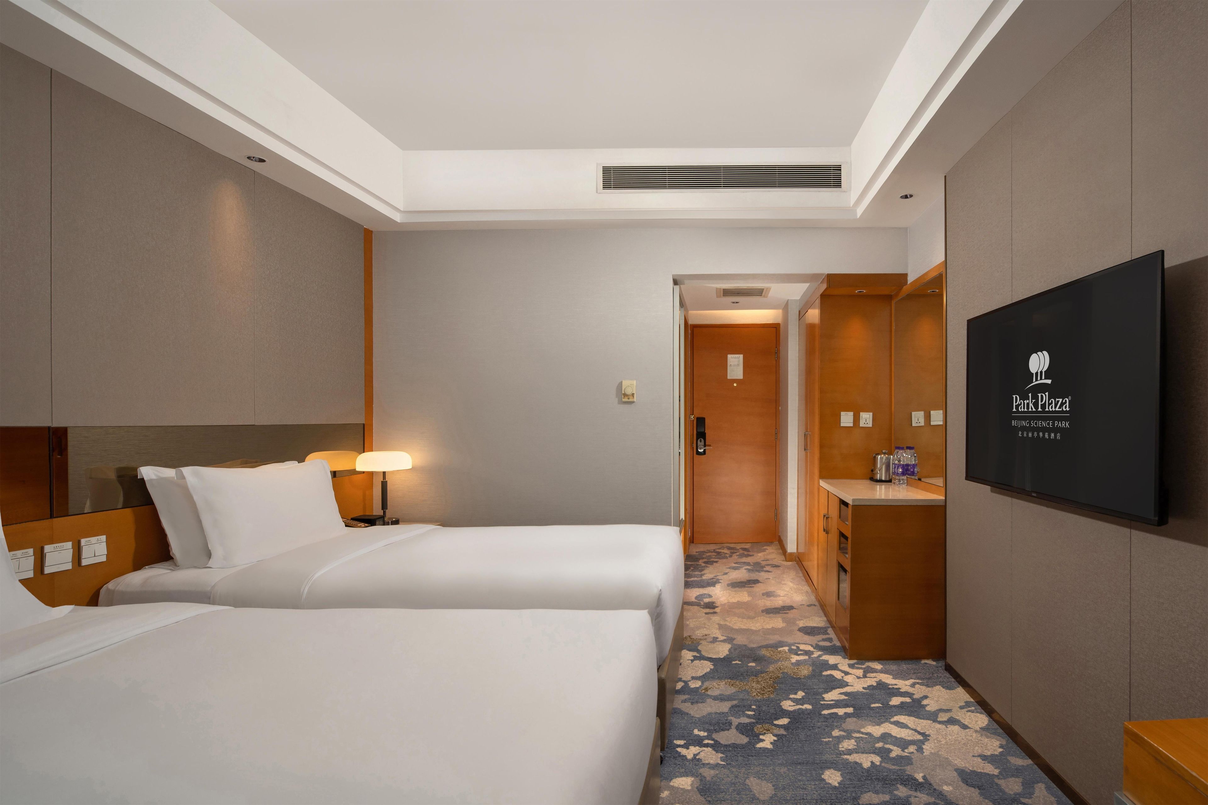A hotel room with two beds, a television, a desk, and a bathroom.