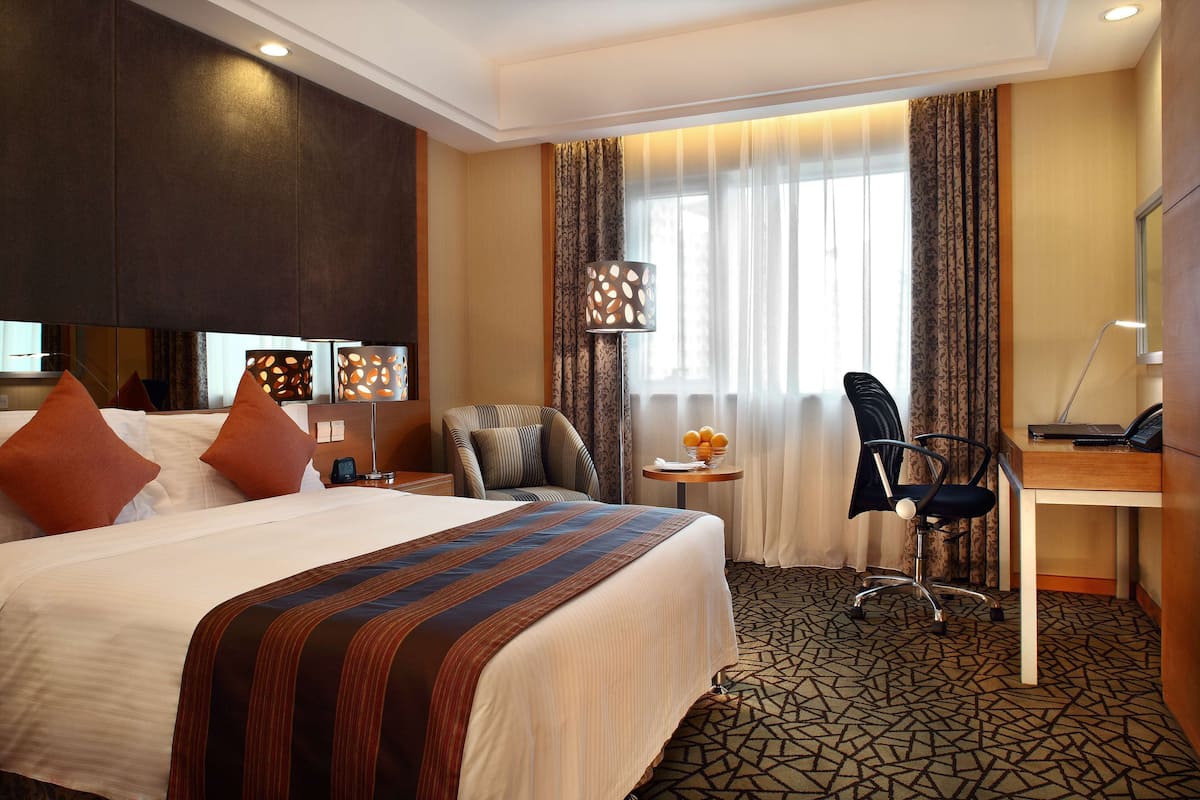 Een hotelkamer met een groot bed, een bureau, een stoel, een lamp en een raam met gordijnen.