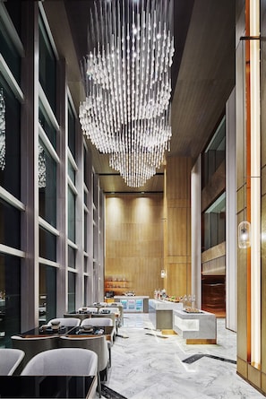 Un vestíbulo moderno de hotel con piso de mármol, un mostrador de recepción central y una araña.