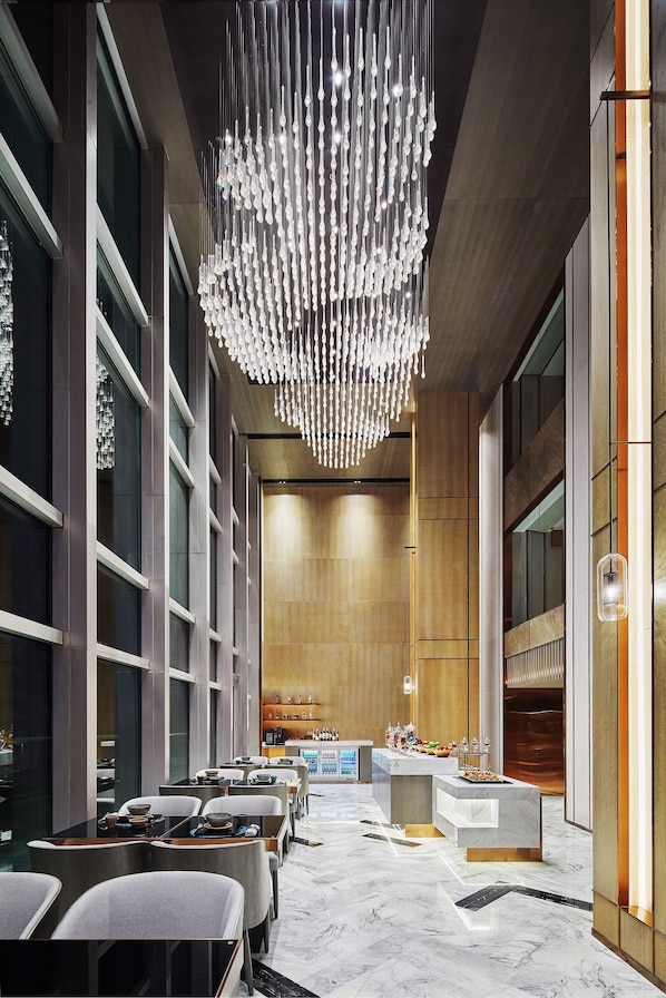 Un vestíbulo moderno de hotel con piso de mármol, un mostrador de recepción central y una araña.
