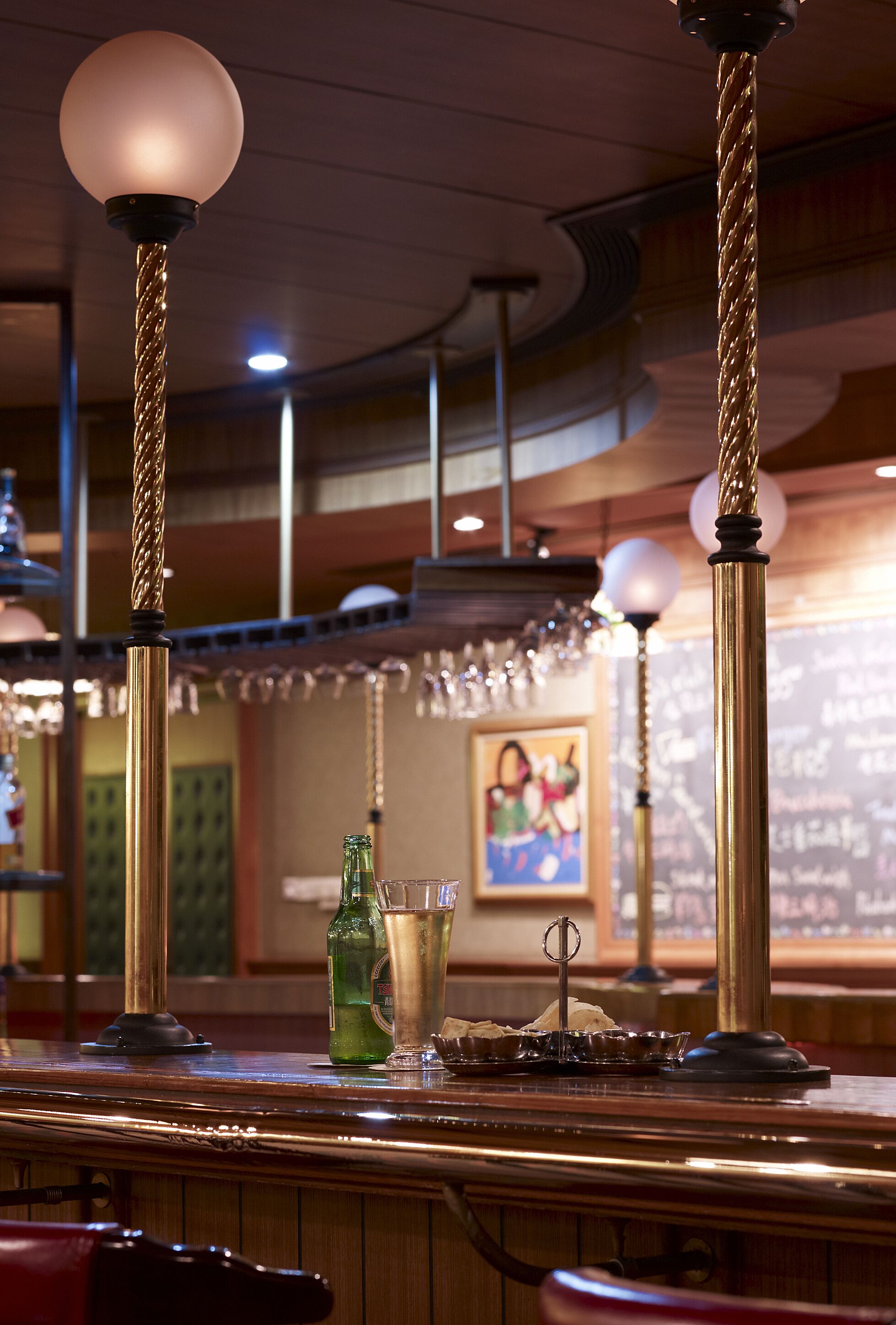 Eine Bar mit einer Holztheke, hängenden Lampen und einem gerahmten Bild an der Wand.