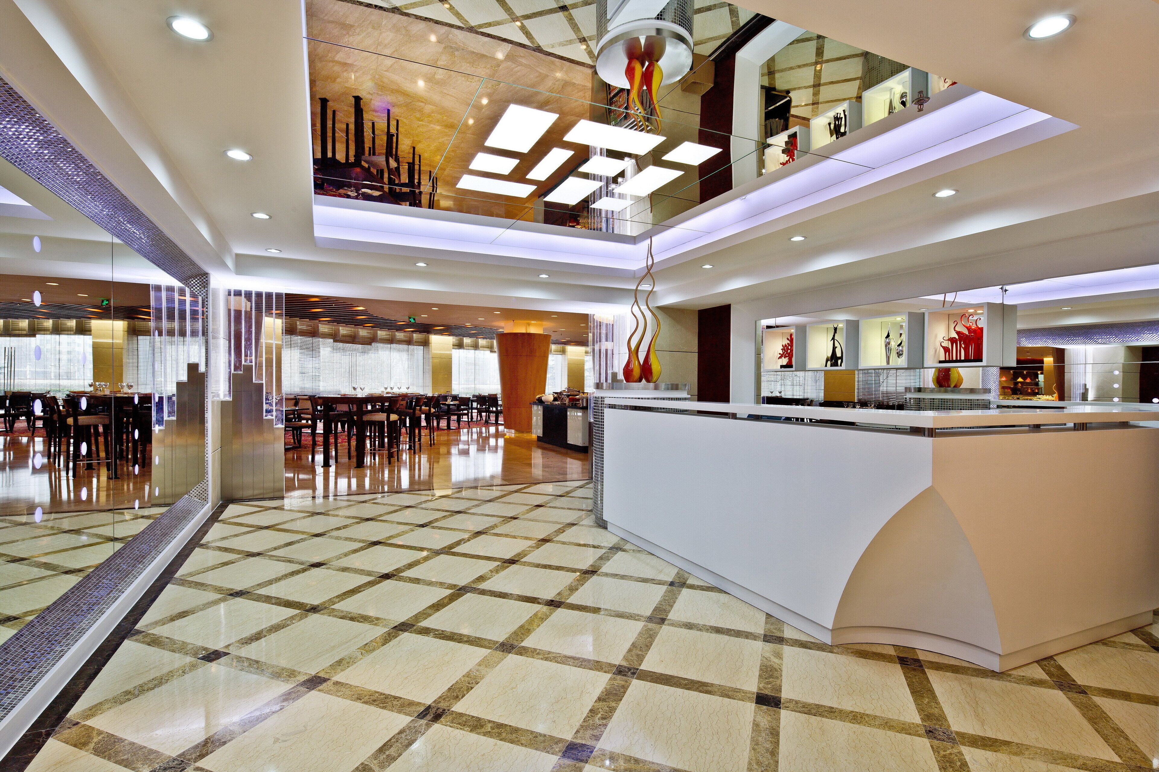 En modern hotellobby med ett rutmönstrat golv, en receptionsdisk och en sittgrupp med bord och stolar.