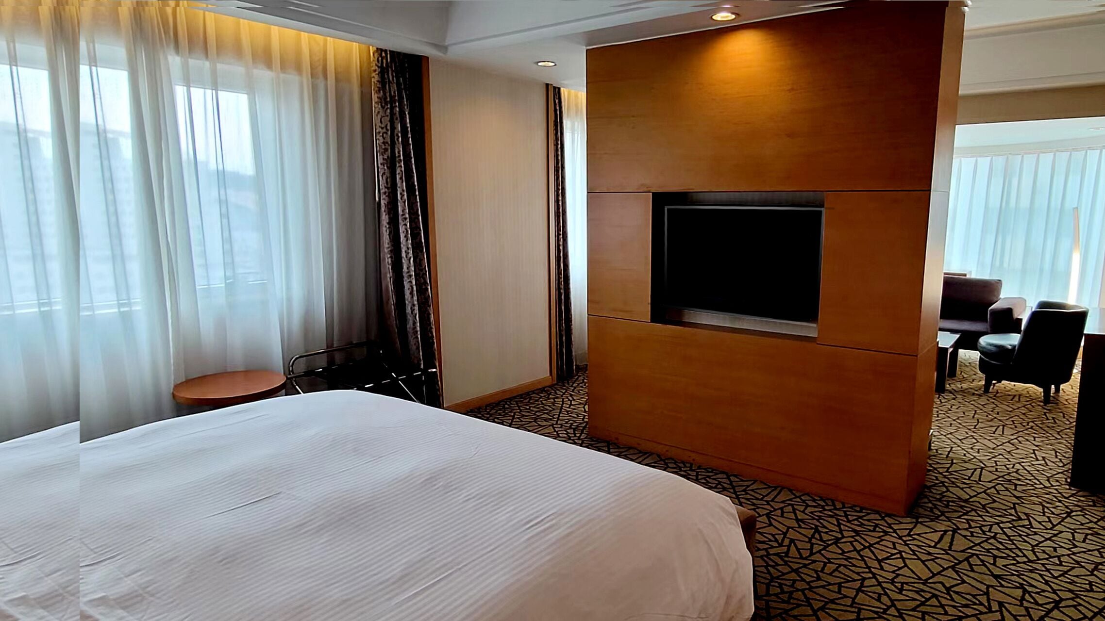 Een hotelkamer met een groot bed, een televisie bevestigd aan een houten paneel, een kleine tafel en een stoel.