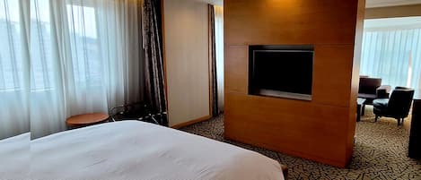 Una habitación de hotel con una cama grande, un televisor montado en un panel de madera, una mesita y una silla.