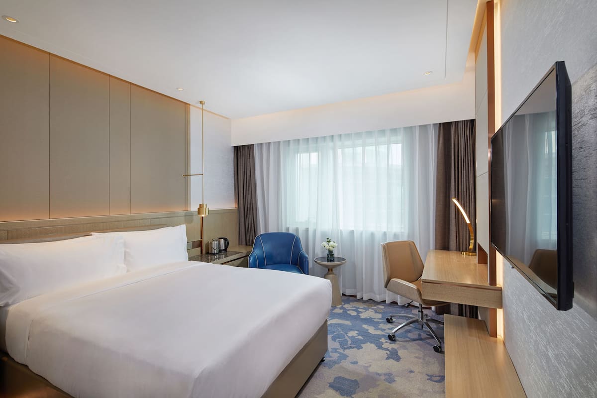 Een hotelkamer met een groot bed, een bureau met stoel, een televisie en een raam met gordijnen.