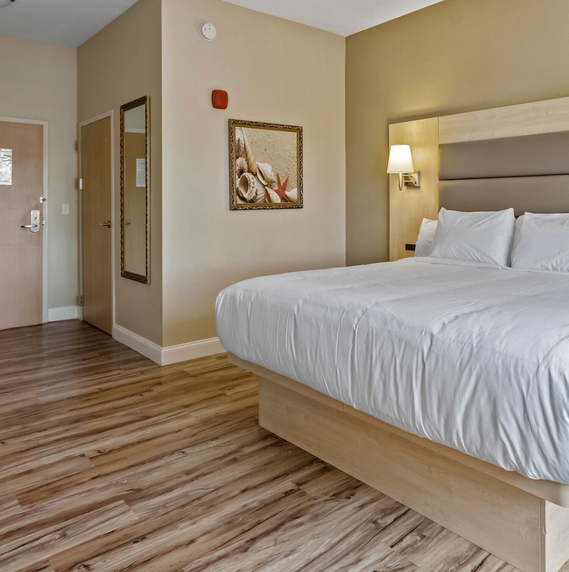 Quarto de hotel com cama grande, piso de madeira, quadro na parede e porta com puxador.