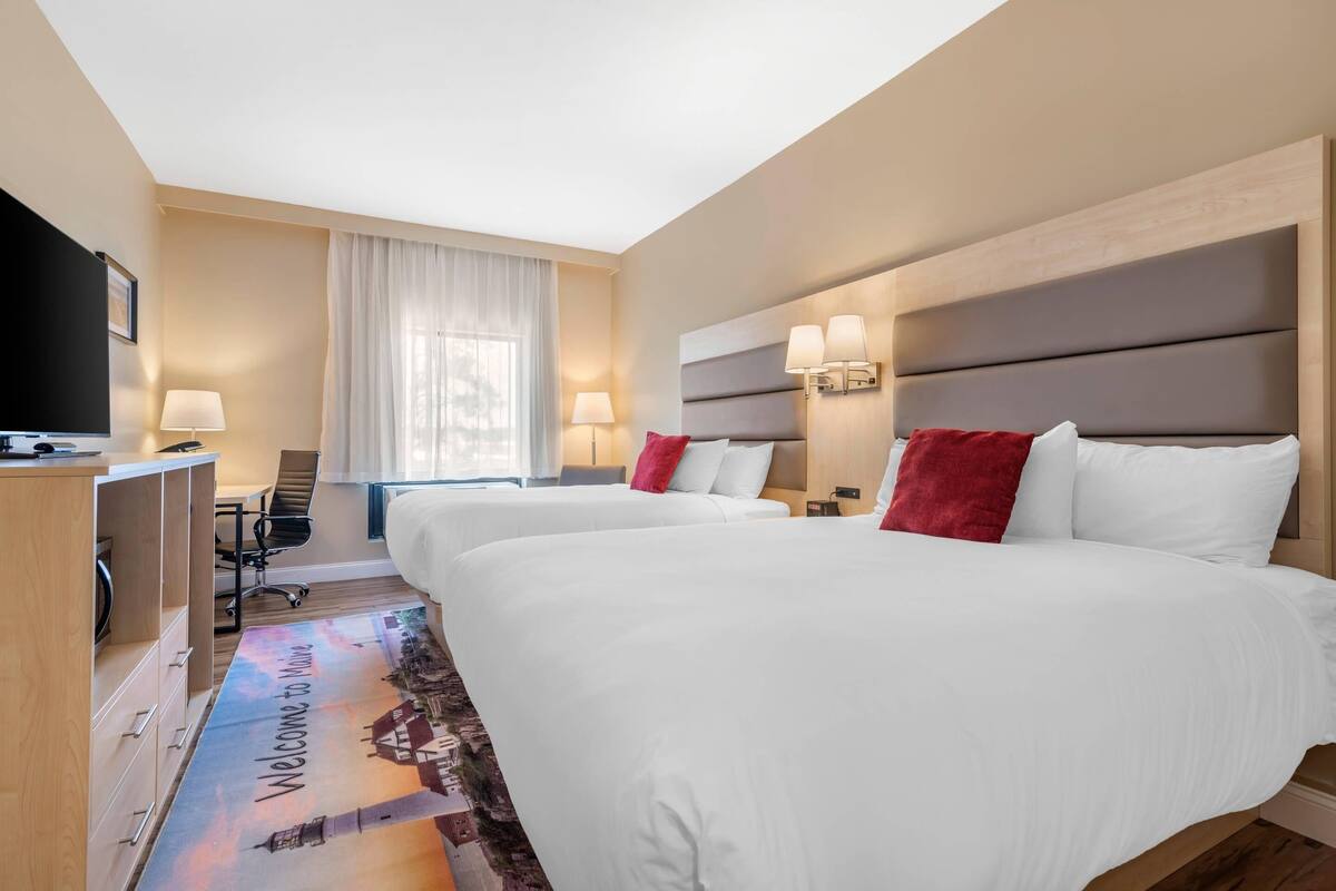 A hotel room with two beds, a desk with a chair, a TV, and a window with curtains.