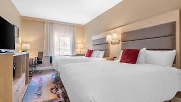 A hotel room with two beds, a desk with a chair, a TV, and a window with curtains.