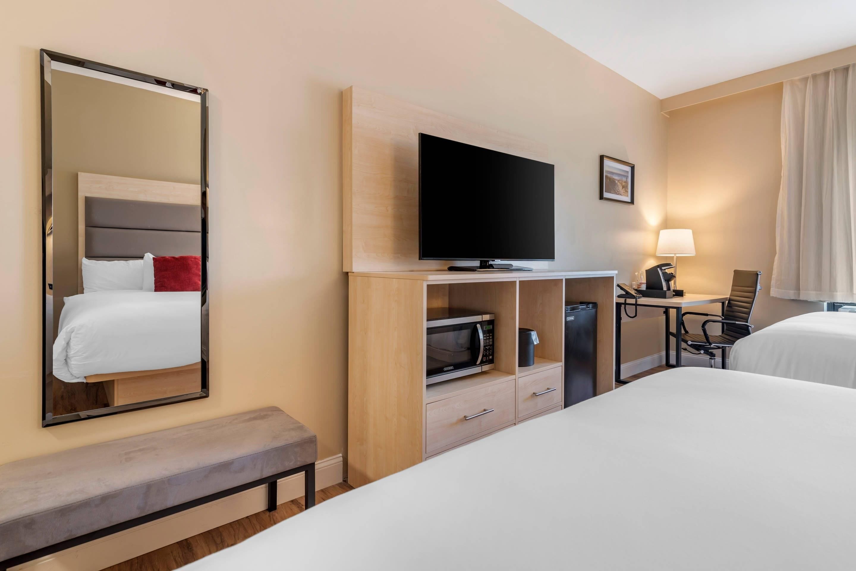 A hotel room with a bed, a TV, a desk with a chair, a microwave, and a lamp.