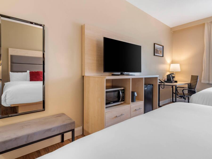 A hotel room with a bed, a TV, a desk with a chair, a microwave, and a lamp.