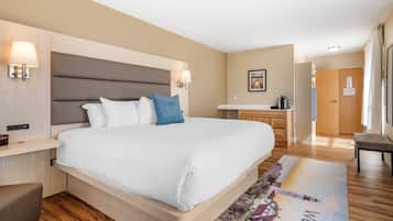 Una habitación de hotel moderna con una cama grande, mesitas de noche, un escritorio pequeño y un baño visible al fondo.