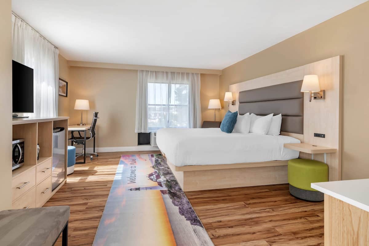 A modern hotel room with a large bed, a desk with a chair, a television, and a window with curtains.