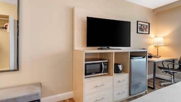 A hotel room with a bed, a desk with a chair, a television, a microwave, a refrigerator, and a bedside table.