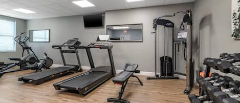 Un gimnasio con cintas de correr, una máquina de remo, un banco de pesas y mancuernas.