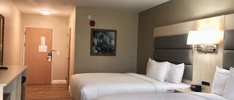 A hotel room with two beds, a painting on the wall, a clock, and a lamp on the nightstand.
