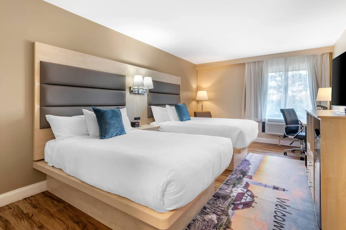 A hotel room with two beds, a desk, a chair, a TV, and a window with curtains.
