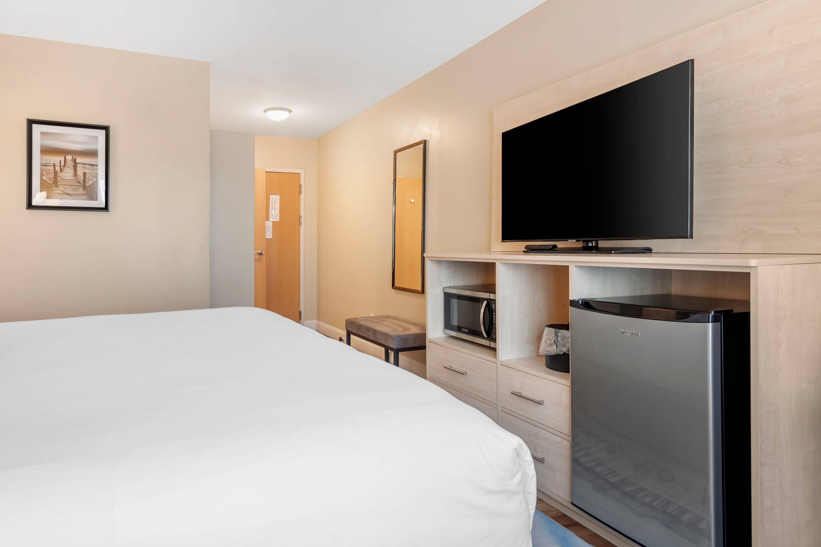 A hotel room with a large bed, a flat-screen TV mounted on a wooden cabinet, a refrigerator, and a microwave.