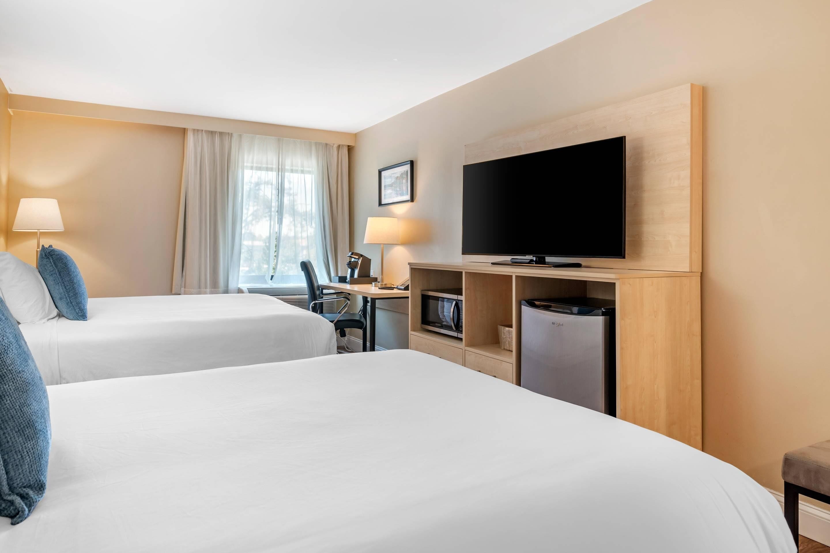 Une chambre d’hôtel avec deux lits, un bureau avec un ordinateur, une télévision et une petite kitchenette.