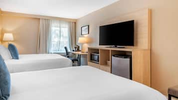 A hotel room with two beds, a desk with a computer, a TV, and a small kitchenette.
