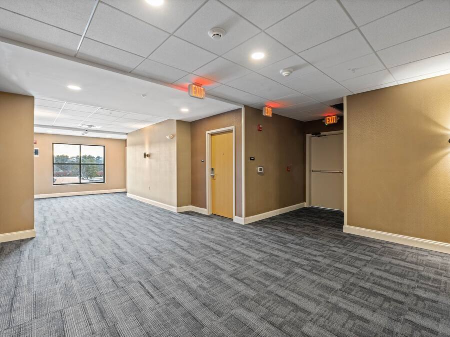 A spacious hallway with carpeted floors, beige walls, and multiple exit signs.