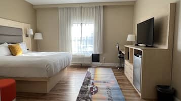 A hotel room with a bed, a desk, a TV, and a window with curtains.