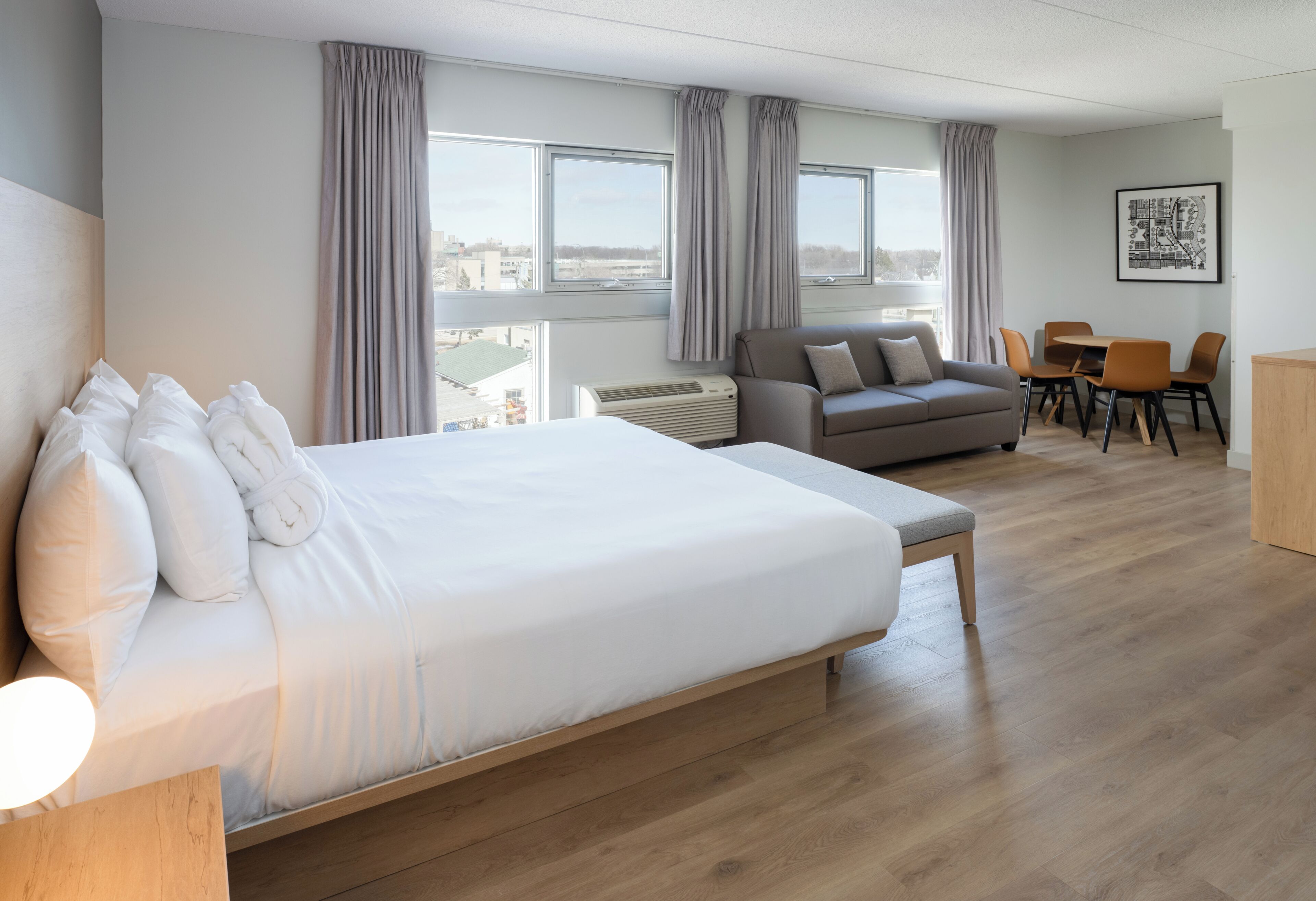 Une chambre d’hôtel dotée d’un grand lit, d’un canapé, d’une table à manger avec des chaises et offrant une vue sur la ville grâce à de grandes fenêtres.