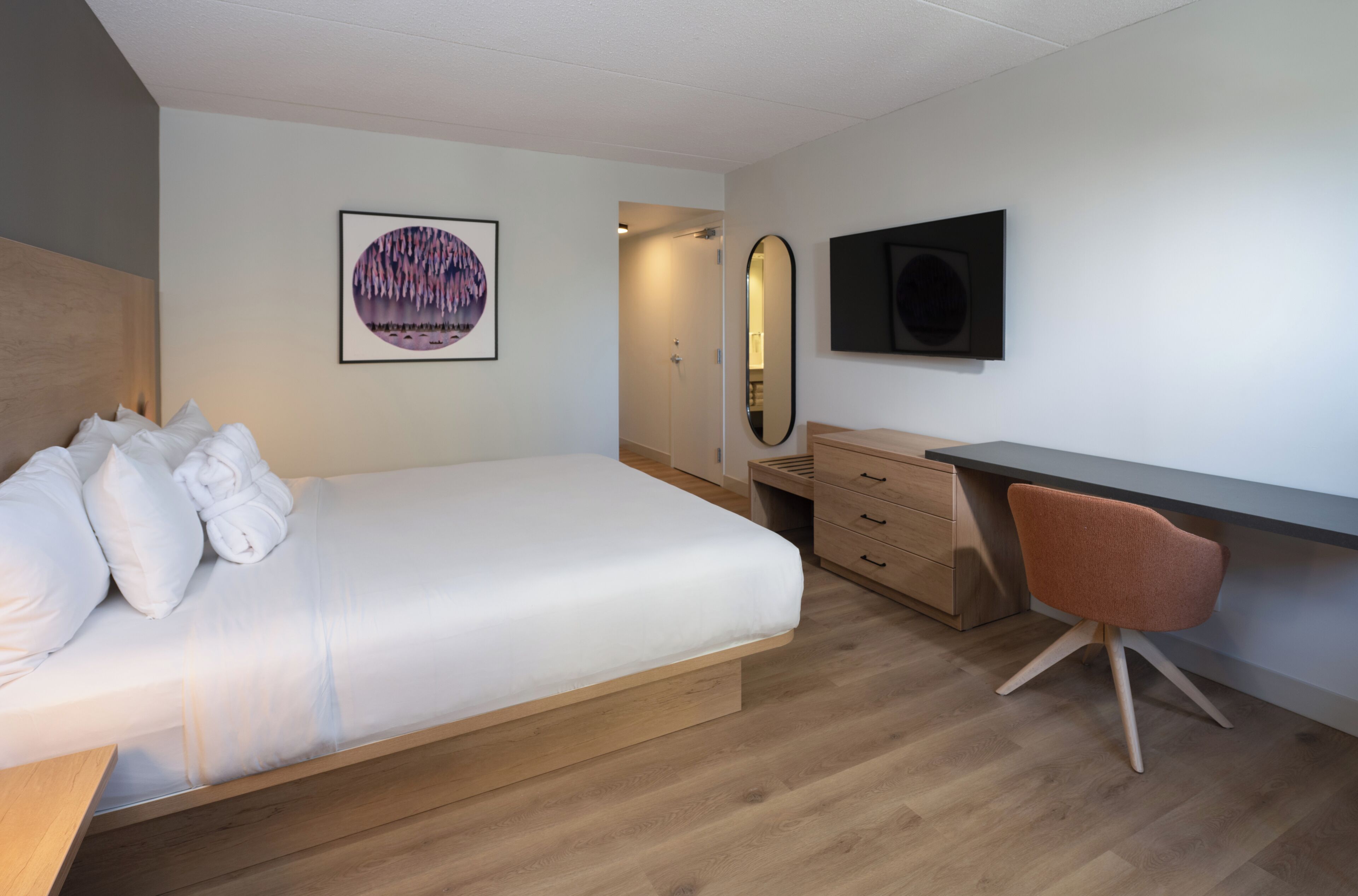 A bedroom with a bed, a desk, a chair, a mirror, and a television.