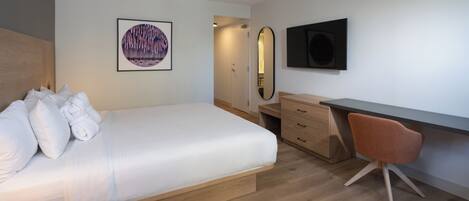 A bedroom with a bed, a desk, a chair, a mirror, and a television.
