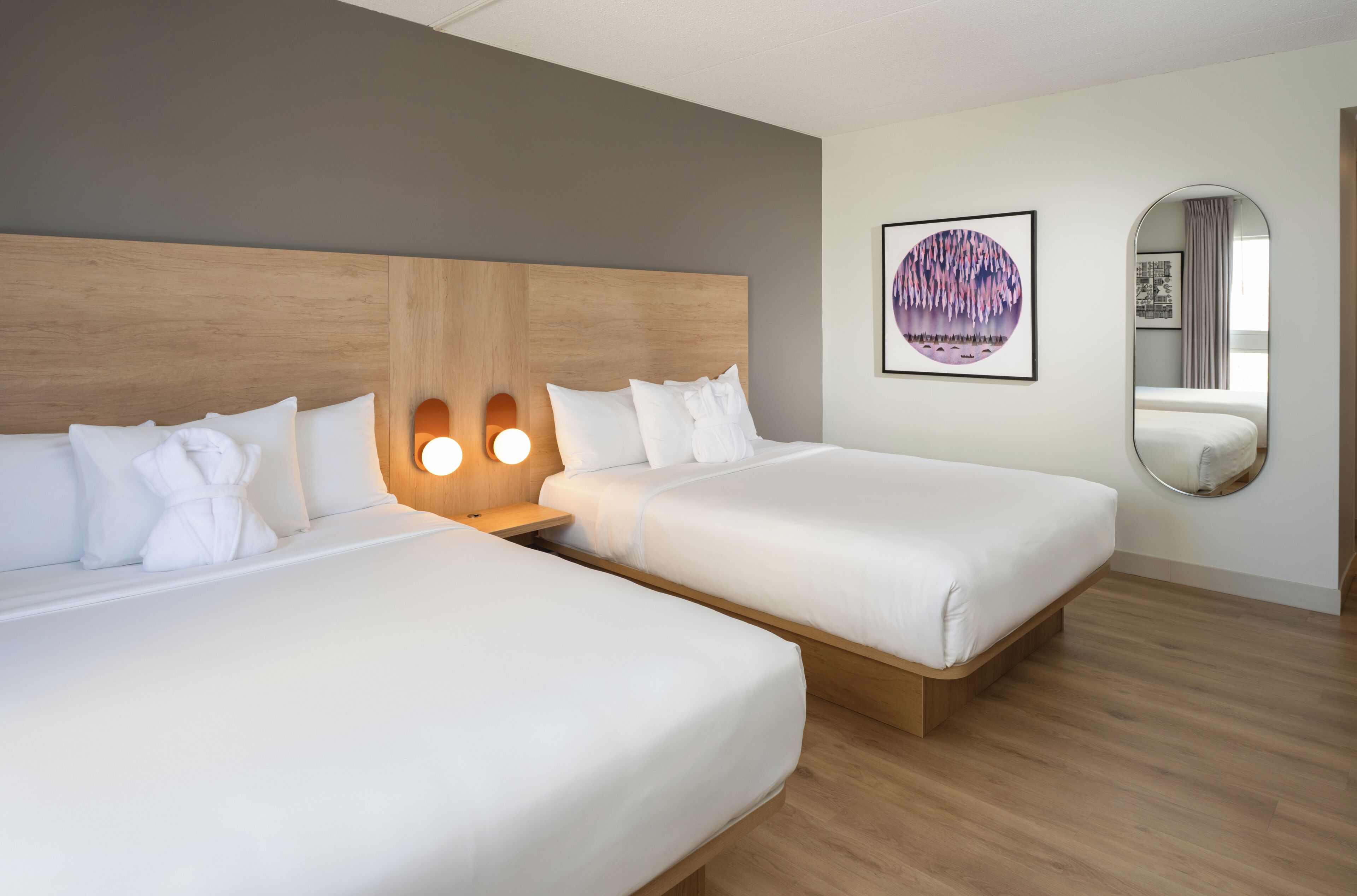 Habitación de hotel con dos camas, cabecero de madera, espejo en la pared y un cuadro enmarcado.