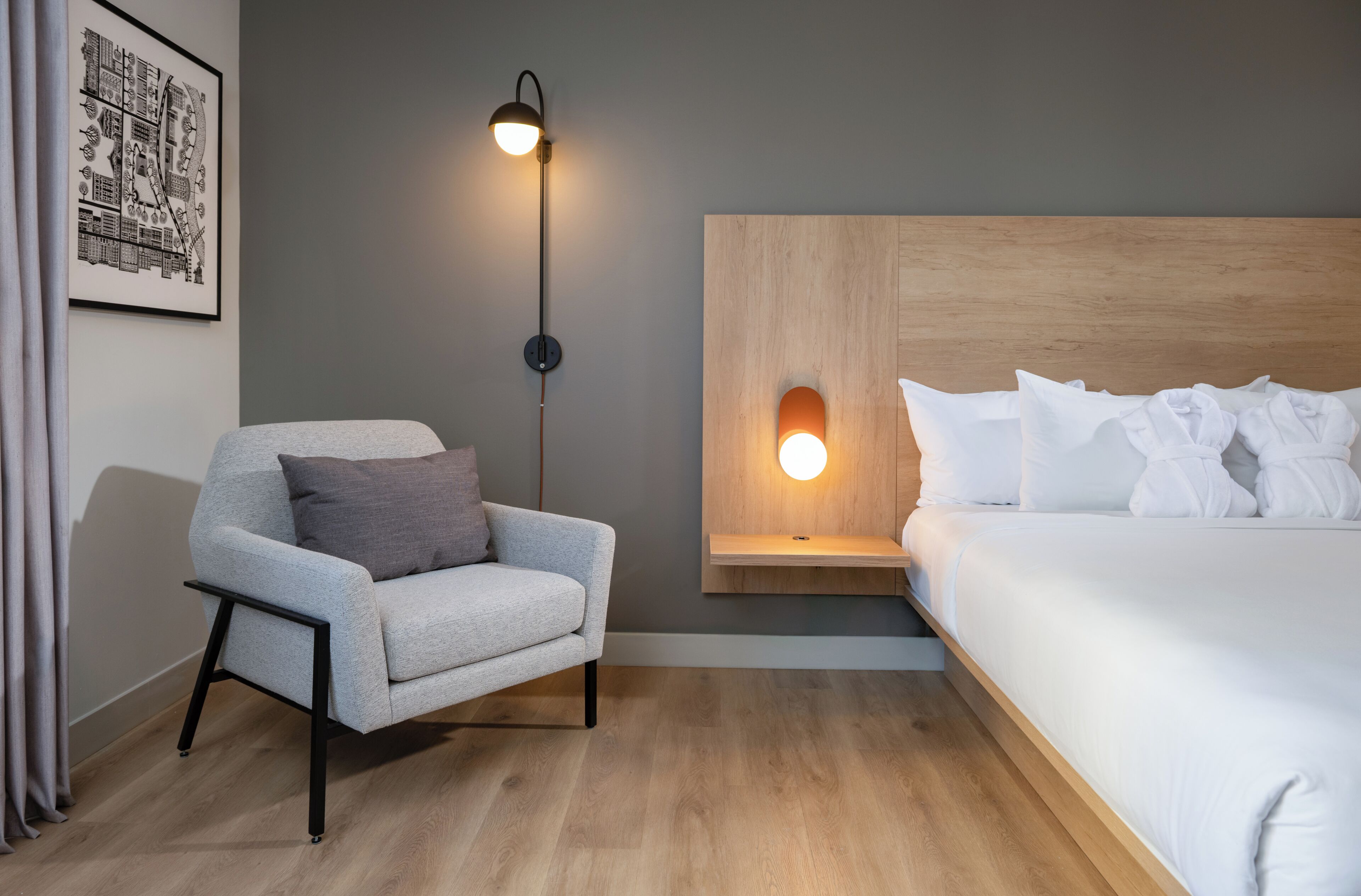 A room with a bed, a chair, a wall-mounted light, and a framed picture.