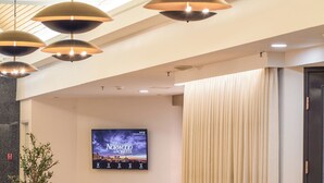 Un vestíbulo con iluminación colgante moderna, un televisor de pantalla plana mostrando el Hotel Norwood y un área de descanso con sillones cómodos.
