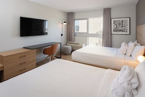 Habitación de hotel con dos camas, un escritorio, una silla, un televisor de pantalla plana, una ventana con cortinas y un mapa enmarcado en la pared.