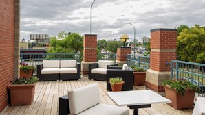 Un patio al aire libre con mobiliario y jardineras, un muro de ladrillo y vistas de la ciudad.