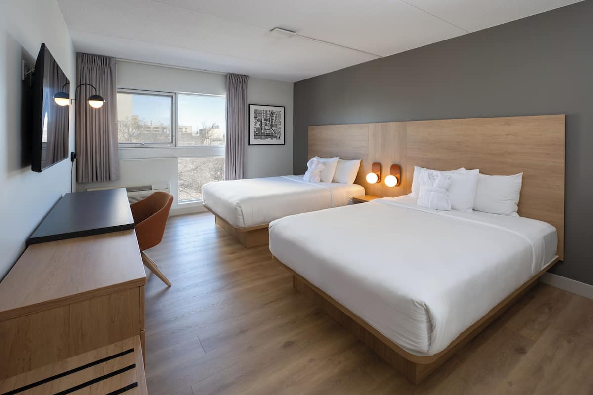 A hotel room with two beds, a desk, a chair, and a window with curtains.
