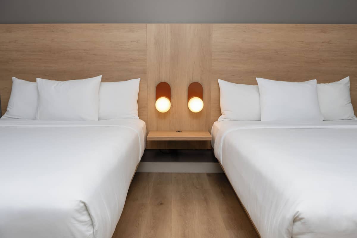 A hotel room with two beds, a wooden headboard, and bedside lamps.