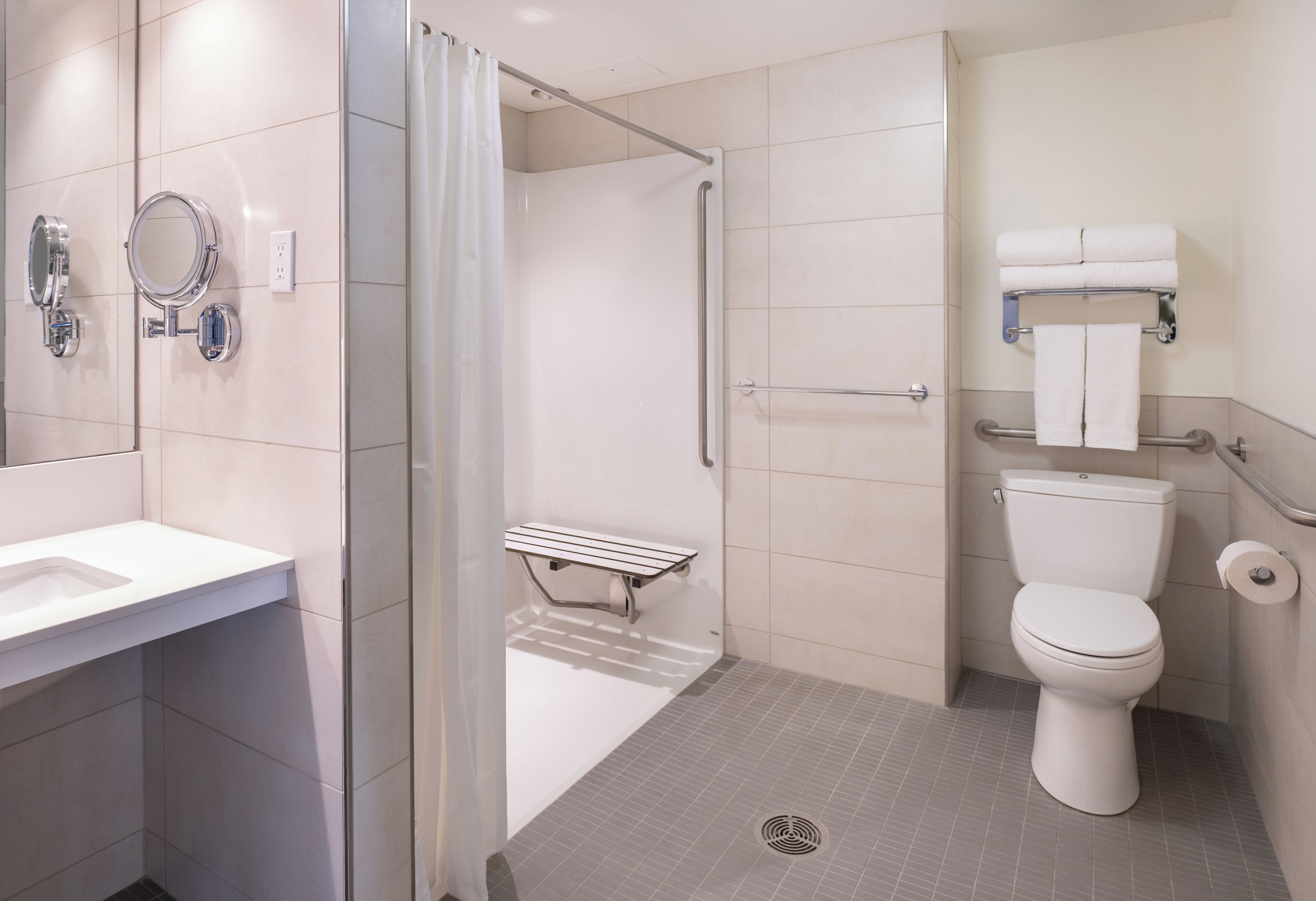 A modern bathroom with a shower, toilet, and sink, equipped with a handrail and a mirror.