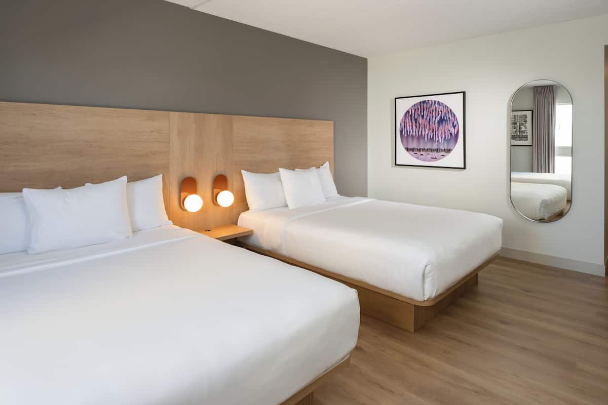 A hotel room with two beds, a wooden headboard, a round mirror, and a framed artwork on the wall.