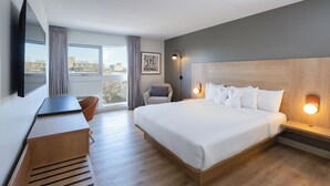 Habitación de hotel con una cama grande, un escritorio, una silla, un televisor y vistas a la ciudad.