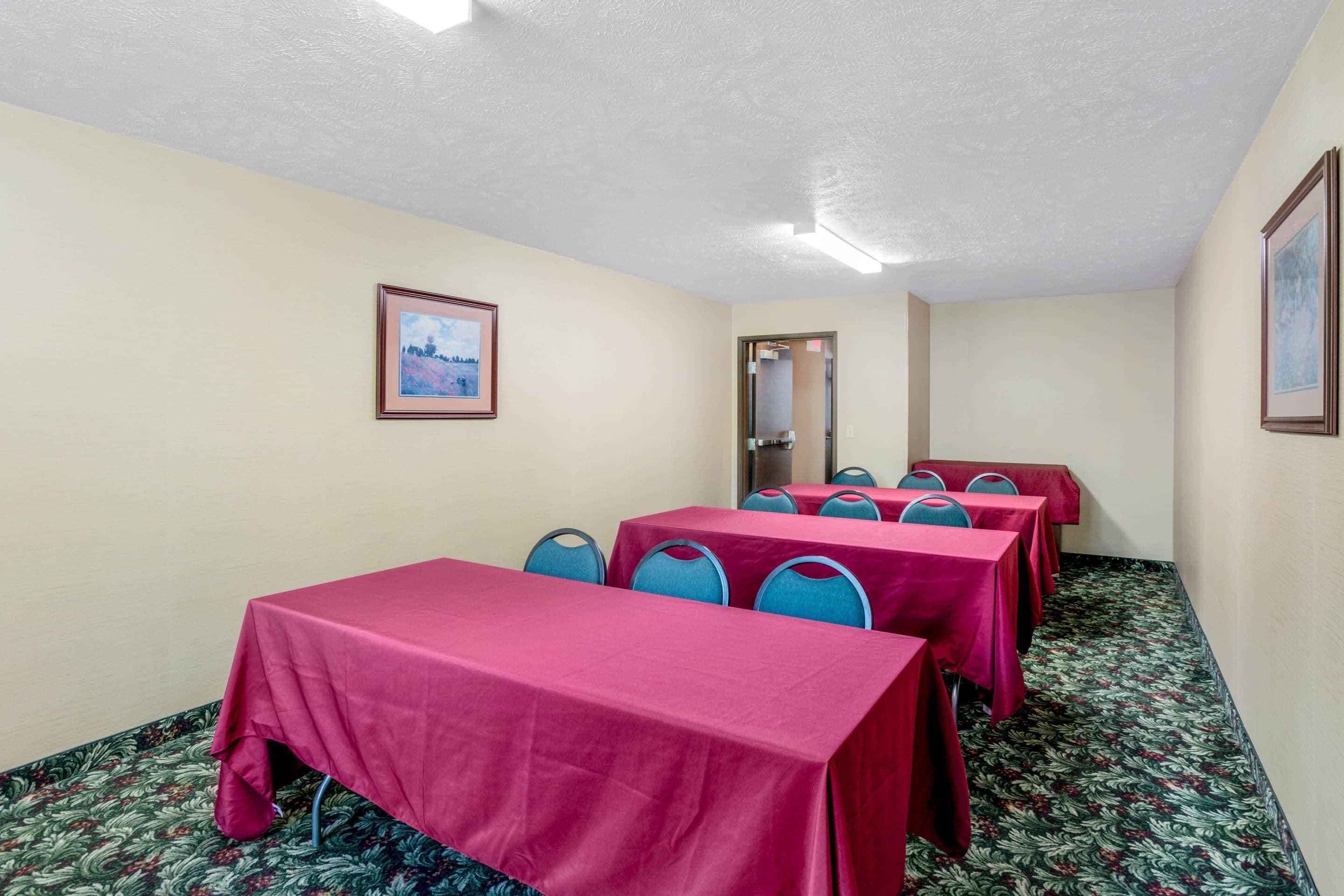 A conference room with tables covered in red tablecloths, blue chairs, and a framed picture on the wall.