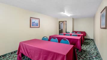 Un salón de conferencias con mesas cubiertas con manteles rojos, sillas azules y un cuadro en la pared.