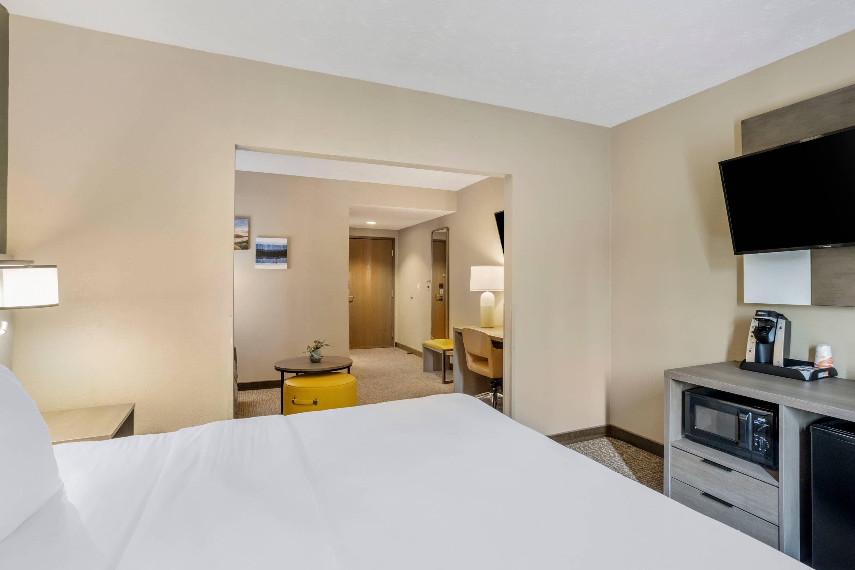 Habitación de hotel con cama, escritorio, silla, televisor y cafetera.
