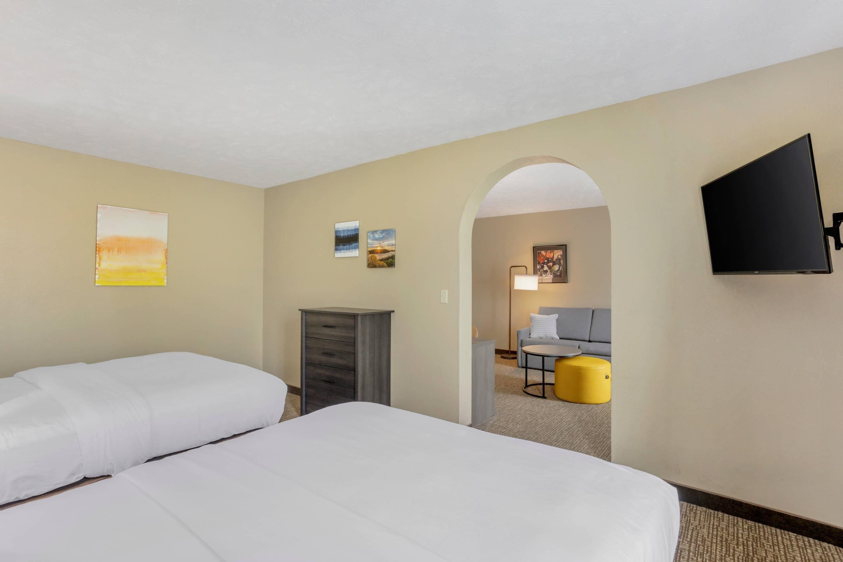 Une chambre d’hôtel avec deux lits, un bureau, une chaise, une télévision et des œuvres d’art accrochées aux murs.